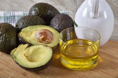 an avocado cut in half next to a glass of oil on a cutting board