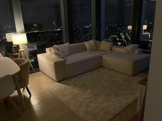 a living room filled with furniture next to tall windows at night time in front of city lights