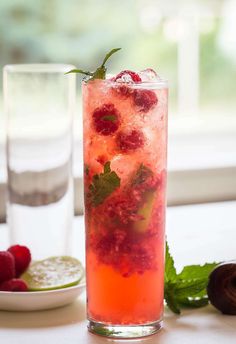 a tall glass filled with ice and raspberries