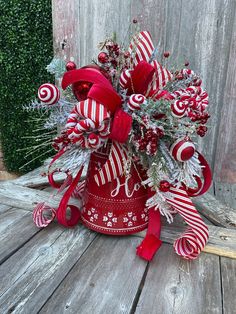 a red christmas bell with candy canes and greenery in it sitting on a wooden table