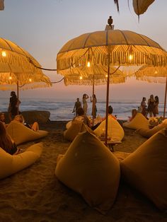 people sitting under umbrellas on the beach at sunset