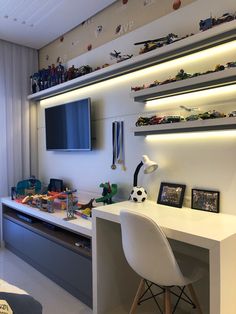 a room with a desk, television and toy cars on the shelves above it is also a wall mounted flat screen tv