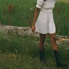 a woman in a white dress and cowboy boots is holding an umbrella over her head