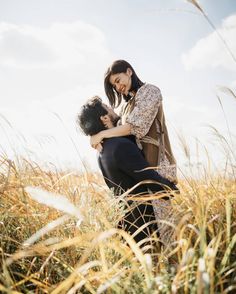 two people standing in tall grass hugging each other