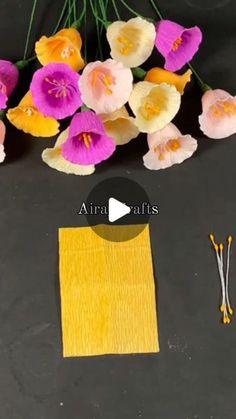 some flowers are sitting on a table next to a yellow piece of paper and thread