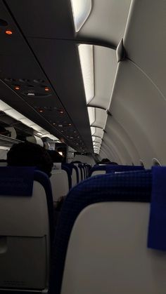 the inside of an airplane with blue seats and white walls, looking down on the aisle