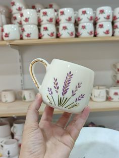 a hand holding a coffee cup with purple flowers painted on the side and gold rim