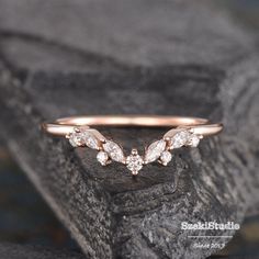 a rose gold wedding band with three diamonds on the top and bottom, sitting on a rock