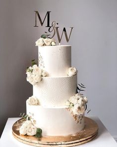 a three tiered wedding cake with white flowers and the initials m & w on top