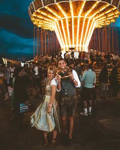 a man and woman standing next to each other in front of a carousel at night