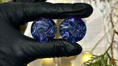 a pair of black gloves holding two purple and blue glass cabochles in front of a christmas tree