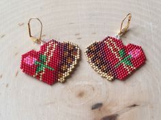 two red heart shaped beaded earrings sitting on top of a wooden table next to each other