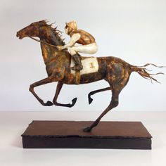 a statue of a man riding a horse on top of a wooden platform with a white wall in the background