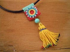 a crocheted necklace with a tassel hanging from it's end on a wooden surface