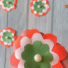 a hand holding a flower made out of felt and paper with other flowers in the background