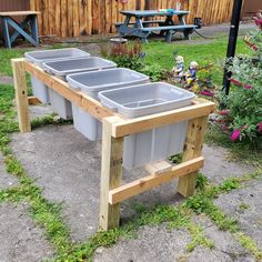 three plastic bins sitting on top of a wooden stand in the grass next to flowers