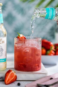 a bottle of alcohol being poured into a glass with strawberries