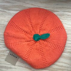 an orange knitted beanie with a green bow on the front and back side