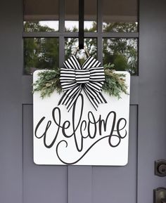 a welcome sign hanging on the front door of a house with wreaths and bow