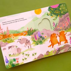 an open children's book with animals and flowers on the cover, sitting on a green surface