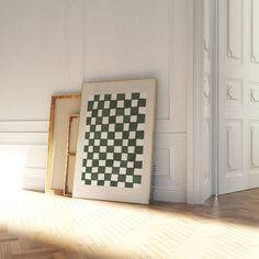 two framed pictures sitting on the floor in front of a wall with a checkerboard pattern