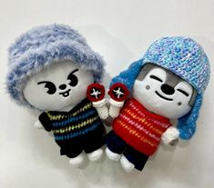 two small stuffed animals wearing hats and sweaters on a white surface with one holding the other's hand