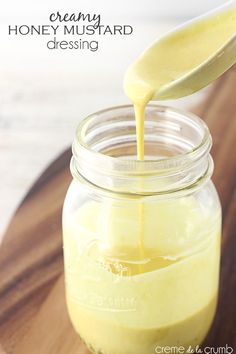 a jar filled with yellow liquid sitting on top of a wooden table next to a spoon