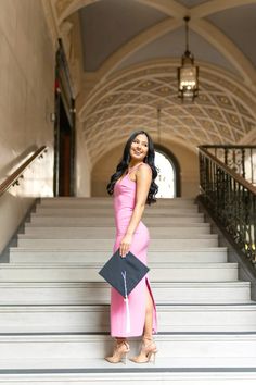 a woman in a pink dress is standing on the stairs with her purse and smiling