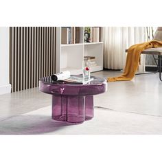 a purple table sitting in the middle of a living room next to a chair and bookshelf