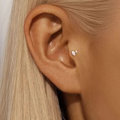 a woman with blonde hair wearing an earring and piercing in the shape of a heart