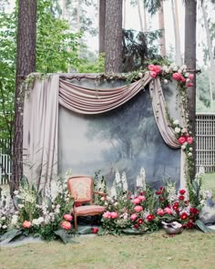 a chair sitting in the middle of a forest filled with flowers and greenery next to a painting