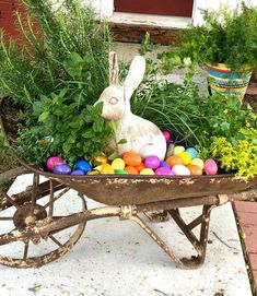 an old wheelbarrow filled with colorful eggs and a white bunny sitting in the center