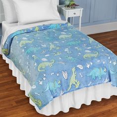 a child's bed with blue and green dinosaur bedspread on top of it