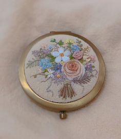 a small compact mirror with flowers on it sitting on a white cloth covered tablecloth