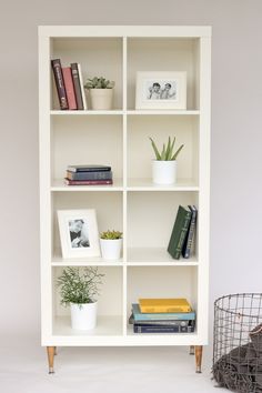 a white shelf with books and plants on it