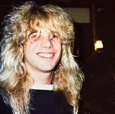 a man with long blonde hair holding up a sign that says vasu - archives