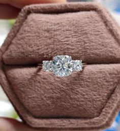 an engagement ring with three diamonds on it in a velvet box that is being held by someone's hand