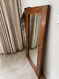 a mirror sitting on top of a floor next to a window with curtains behind it