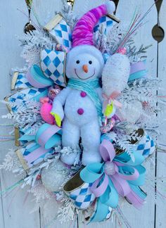 a snowman wreath hanging on the side of a white wooden door with blue and pink ribbons