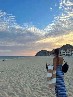 a woman standing on top of a sandy beach under a blue and white cloudy sky