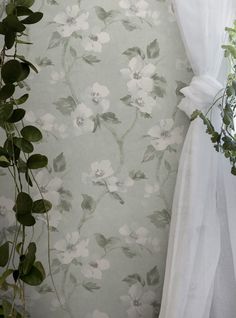 white flowers and greenery are on the wall next to a window with sheer curtains