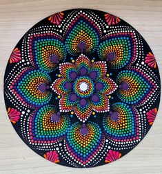 a colorful painting on a wooden surface with circles and dots in the center, as well as an abstract flower design