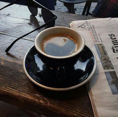 a cup of coffee sitting on top of a black saucer next to a newspaper