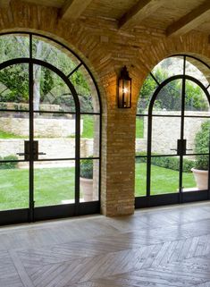 an empty room with large arched windows and wood flooring on the outside, overlooking a garden