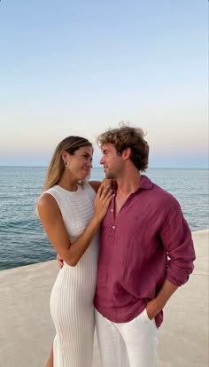 a man and woman standing next to each other on the beach with water in the background