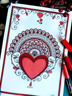 a red heart on a white card surrounded by crayon markers and colored pencils