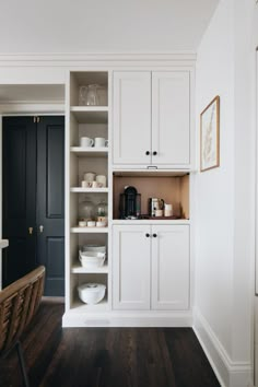 a kitchen with white cupboards and black doors in the center, along with wooden flooring