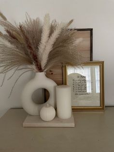 a white vase sitting on top of a table next to a framed photo and some feathers