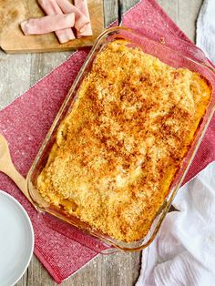 a casserole dish with meat and cheese in it on a red towel next to two white plates