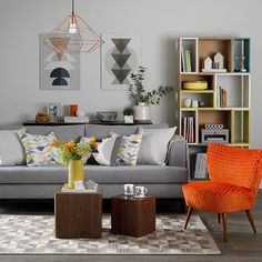 a living room with grey couches and orange chairs in front of bookshelves